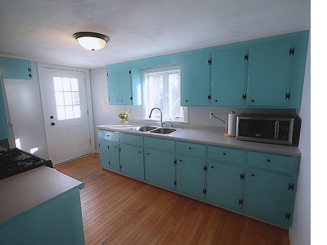 kitchen with a sink, light countertops, light wood-type flooring, a wealth of natural light, and stainless steel microwave