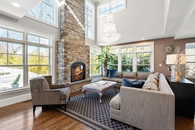 living area with a notable chandelier, a stone fireplace, baseboards, and wood finished floors