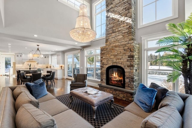 living room with a notable chandelier, plenty of natural light, wood finished floors, and a stone fireplace