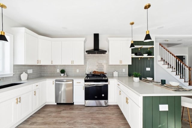 kitchen featuring a kitchen breakfast bar, hanging light fixtures, kitchen peninsula, stainless steel appliances, and wall chimney exhaust hood