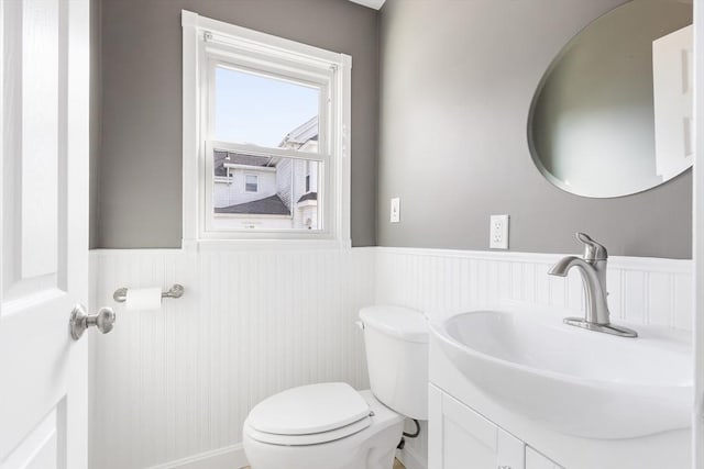 half bath featuring wainscoting, toilet, and vanity