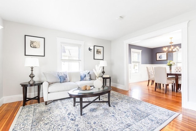 living area featuring baseboards, light wood-type flooring, plenty of natural light, and an inviting chandelier