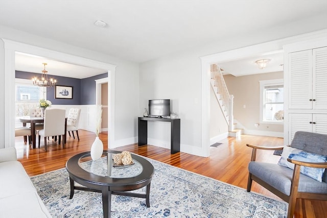 living area with visible vents, wood finished floors, baseboards, a chandelier, and stairs