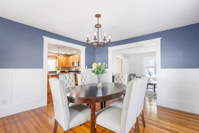 dining space featuring an inviting chandelier, wainscoting, and light wood finished floors