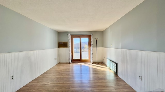 empty room featuring an AC wall unit, radiator, light hardwood / wood-style flooring, and a textured ceiling