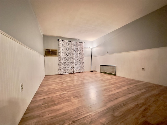 additional living space with a wall mounted air conditioner, wood-type flooring, and vaulted ceiling