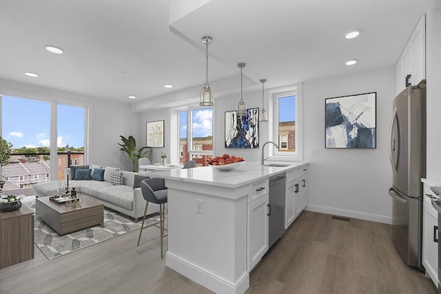 kitchen with appliances with stainless steel finishes, white cabinetry, kitchen peninsula, light hardwood / wood-style flooring, and decorative light fixtures