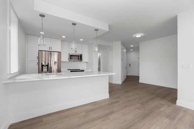 kitchen featuring white cabinets, hanging light fixtures, kitchen peninsula, appliances with stainless steel finishes, and light hardwood / wood-style floors