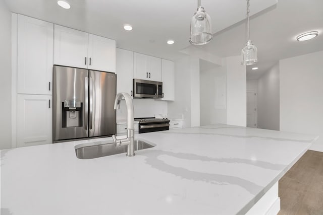 kitchen with light stone counters, white cabinets, hanging light fixtures, sink, and appliances with stainless steel finishes