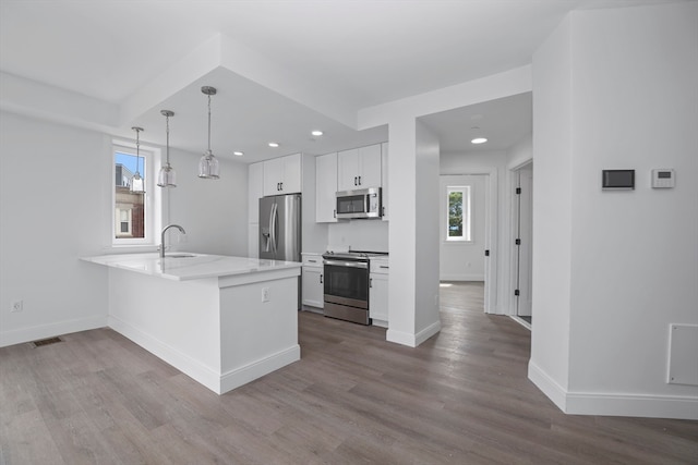 kitchen with white cabinets, kitchen peninsula, appliances with stainless steel finishes, and hardwood / wood-style floors