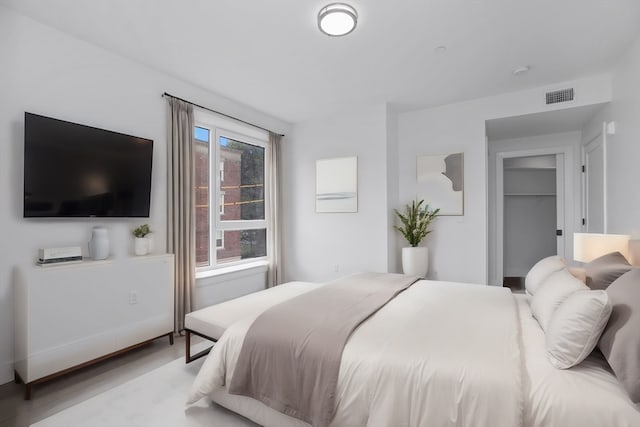 bedroom with a spacious closet, a closet, light hardwood / wood-style floors, and multiple windows