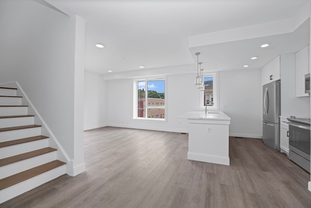 kitchen featuring wood-type flooring, white cabinets, hanging light fixtures, a kitchen island, and appliances with stainless steel finishes