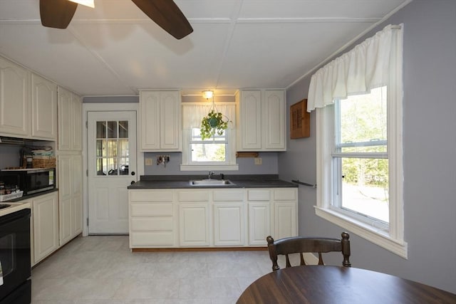 kitchen with a sink, stainless steel microwave, a ceiling fan, dark countertops, and range with electric cooktop