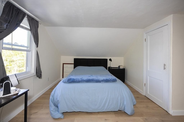 bedroom with vaulted ceiling, baseboards, and light wood finished floors