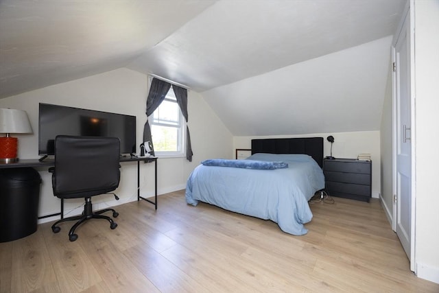 bedroom featuring light wood-style floors, vaulted ceiling, an office area, and baseboards