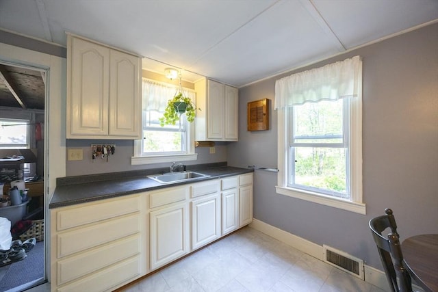 kitchen featuring a sink, dark countertops, plenty of natural light, and baseboards