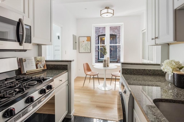 kitchen with appliances with stainless steel finishes, washer / dryer, dark stone countertops, and white cabinetry