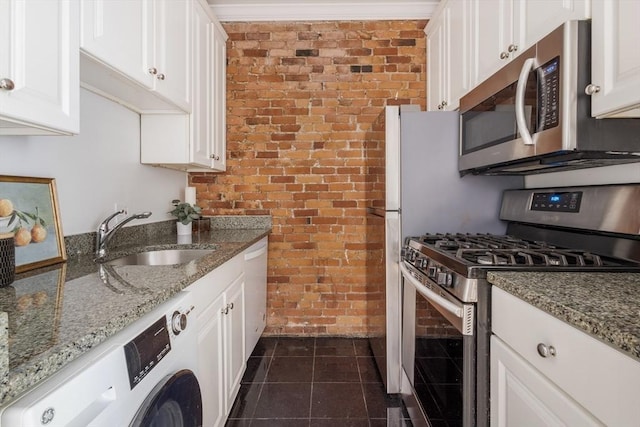 kitchen with stainless steel appliances, brick wall, a sink, white cabinetry, and stone countertops