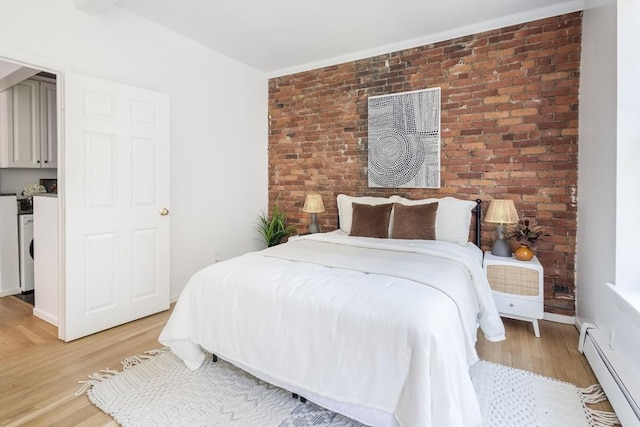 bedroom featuring a baseboard heating unit, light wood-style floors, brick wall, and washer / clothes dryer