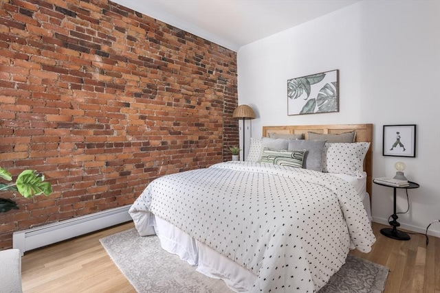bedroom featuring a baseboard heating unit, brick wall, wood finished floors, and baseboards