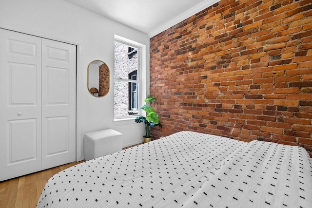 bedroom with brick wall, wood finished floors, and a closet
