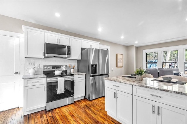 kitchen featuring tasteful backsplash, wood-type flooring, white cabinetry, and appliances with stainless steel finishes