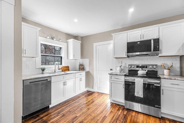 kitchen with light stone counters, white cabinetry, backsplash, stainless steel appliances, and wood-type flooring