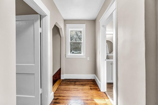 hall with a sink, baseboards, and wood finished floors