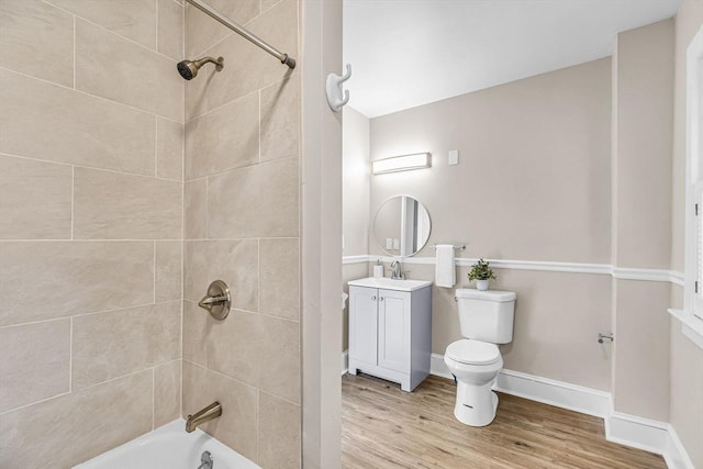 bathroom featuring vanity, toilet, wood finished floors, washtub / shower combination, and baseboards