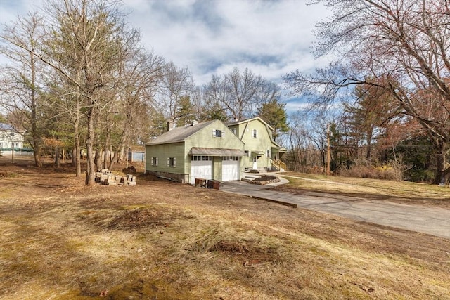 view of side of home featuring aphalt driveway, a gambrel roof, a chimney, and an attached garage