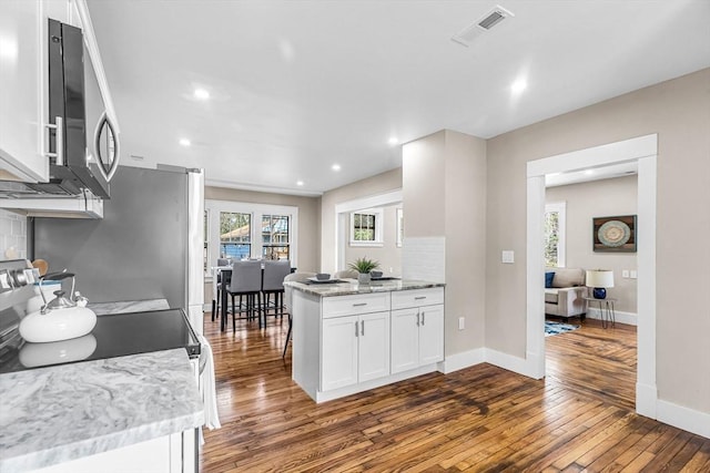 kitchen featuring stainless steel microwave, baseboards, white cabinetry, dark wood-type flooring, and visible vents