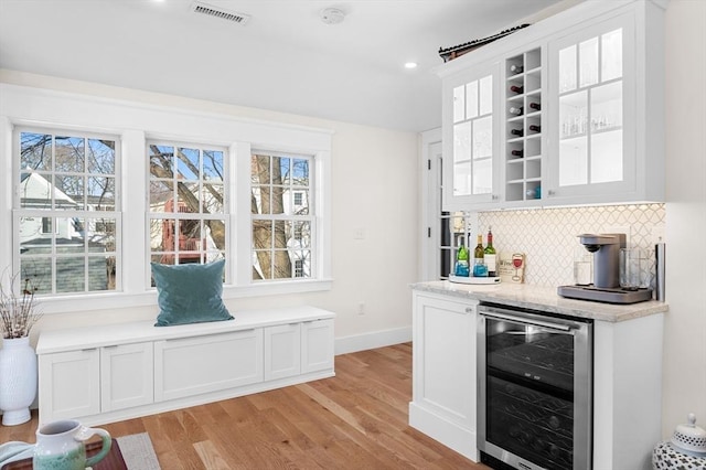 bar featuring a dry bar, beverage cooler, visible vents, decorative backsplash, and light wood-style floors