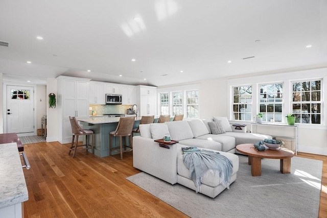 living room with light wood-type flooring, visible vents, baseboards, and recessed lighting