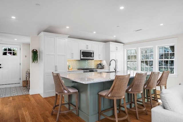 kitchen featuring light wood finished floors, visible vents, stainless steel microwave, stove, and a sink