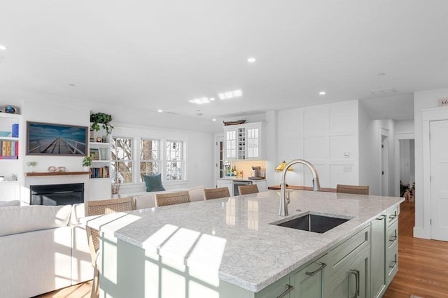 kitchen featuring an island with sink, wood finished floors, light stone countertops, a fireplace, and a sink