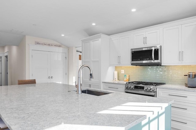 kitchen featuring an island with sink, decorative backsplash, stainless steel appliances, and a sink