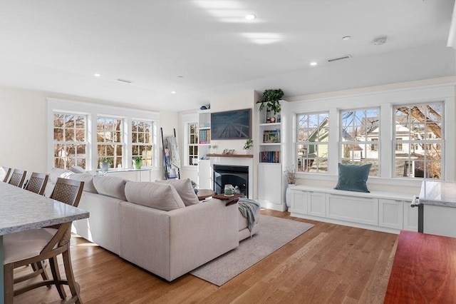 living room with light wood-type flooring, a fireplace, visible vents, and recessed lighting