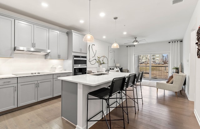 kitchen with double oven, gray cabinets, a kitchen island with sink, and sink