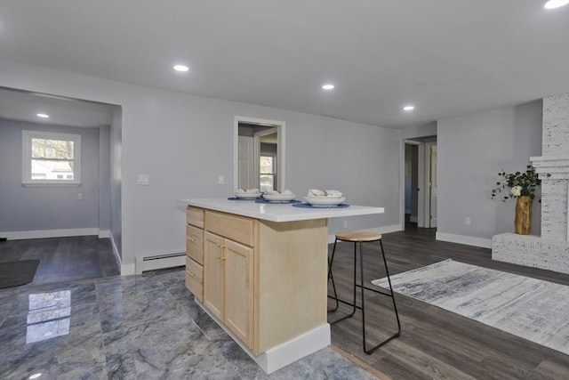 kitchen with a breakfast bar area, baseboard heating, light countertops, baseboards, and light brown cabinets