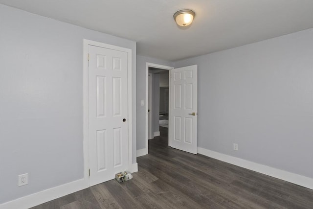 unfurnished bedroom featuring baseboards, dark wood-style flooring, and a closet