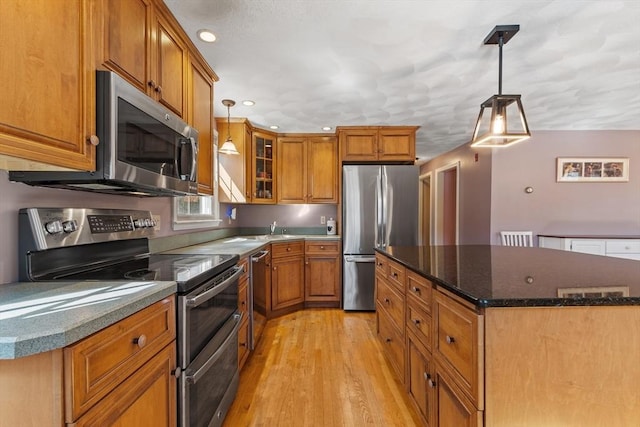 kitchen featuring a center island, glass insert cabinets, hanging light fixtures, appliances with stainless steel finishes, and brown cabinetry