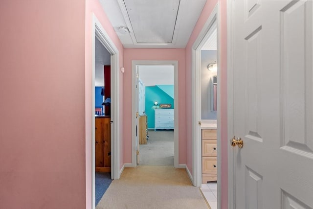 hall with attic access, light colored carpet, and baseboards