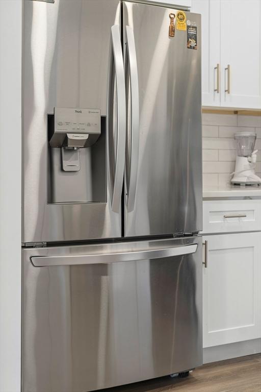 details featuring decorative backsplash, light hardwood / wood-style floors, white cabinetry, and stainless steel refrigerator with ice dispenser