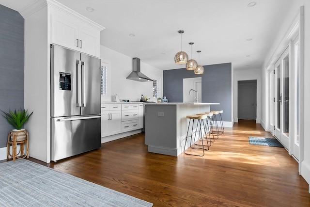 kitchen with wood finished floors, high end fridge, a center island with sink, wall chimney exhaust hood, and white cabinets