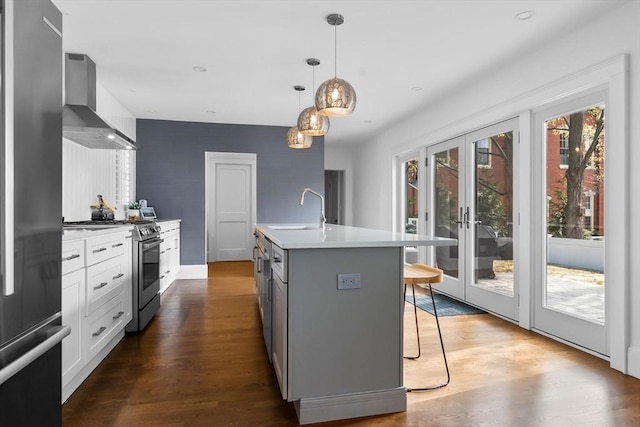 kitchen with wall chimney range hood, appliances with stainless steel finishes, a sink, a kitchen island with sink, and a breakfast bar area