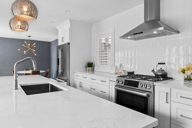 kitchen featuring wall chimney range hood, white cabinets, appliances with stainless steel finishes, light stone counters, and a sink