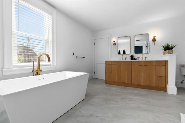 full bathroom featuring double vanity, a freestanding tub, toilet, and a wealth of natural light