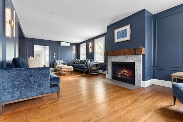 living area with wood finished floors, a wall mounted AC, a decorative wall, and a fireplace