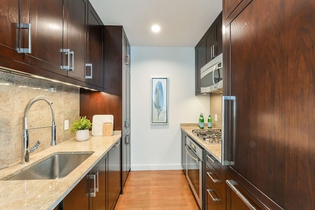 kitchen featuring a sink, stainless steel appliances, light wood-type flooring, and light stone counters