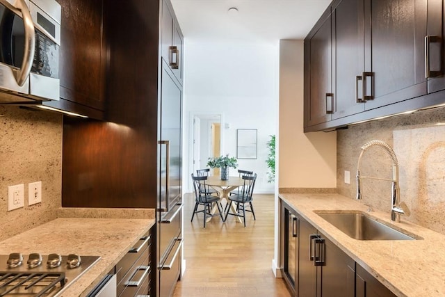 kitchen with light stone counters, a sink, stainless steel appliances, light wood-type flooring, and backsplash